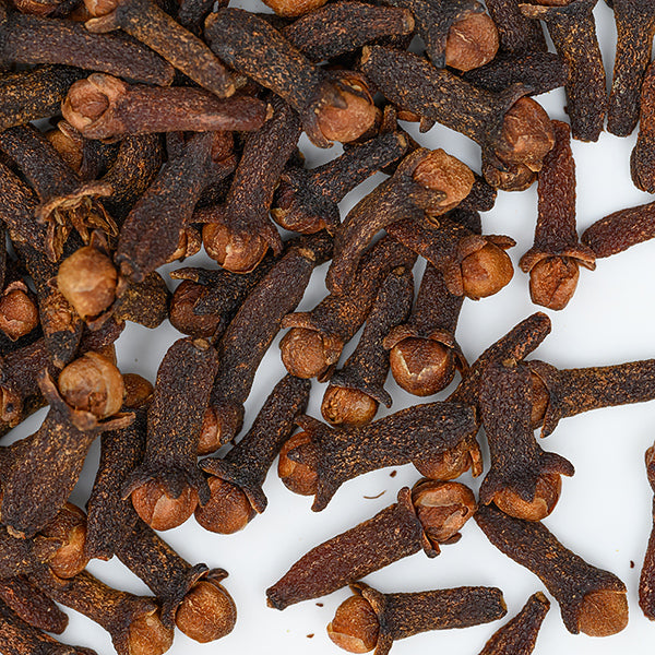 A close-up of Cloves Whole Organic by Whole Spice Inc. shows dried flower buds scattered on white, highlighting their dark brown stems and lighter tops.