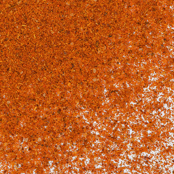 Close-up of Whole Spice Inc. Ethiopian Berbere Spice scattered on a white background, highlighting its reddish-orange color and mixed granules—a key ingredient in Ethiopian lentil stews and other spicy dishes.