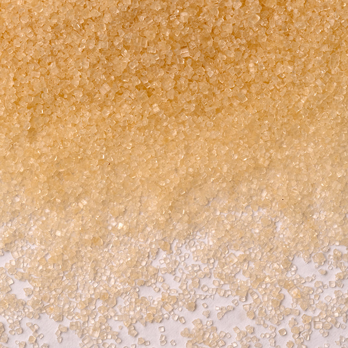 Close-up of Whole Spice Inc. Evaporated Cane Sugar: raw, golden crystals scattered on white. The coarse granules vary in size, making them an excellent substitute for refined sugar.
