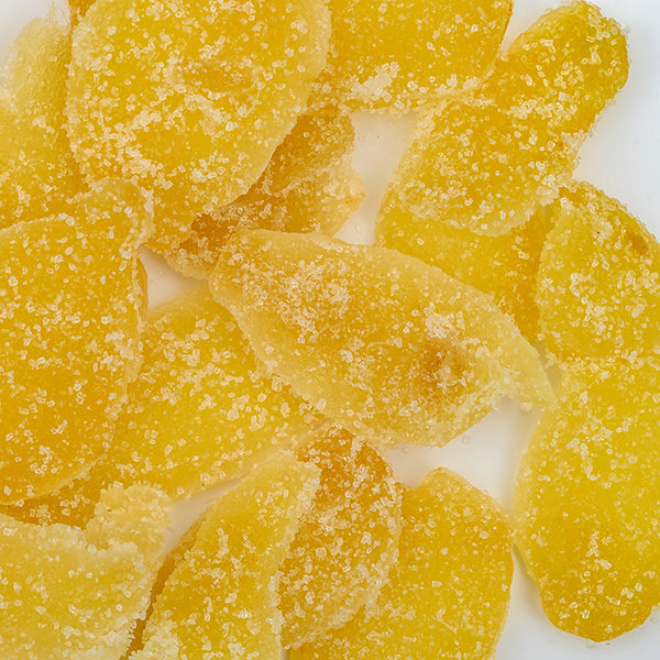 Close-up of Ginger Crystallized by Whole Spice Inc., arranged with several pieces of granulated sugar-coated dried mango slices on a white background.