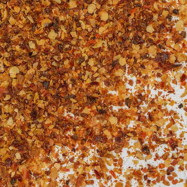 Close-up of Whole Spice Inc. Habanero Chili Crushed flakes scattered on a white surface, featuring vibrant hot chili pepper pieces and seeds that showcase the intense heat typical of habaneros.