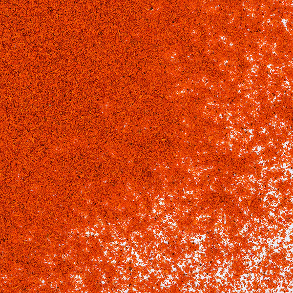A close-up of Whole Spice Inc. Hot Smoked Paprika powder in a vibrant orange-red tone, scattered unevenly on a white surface for a rich, textured look.