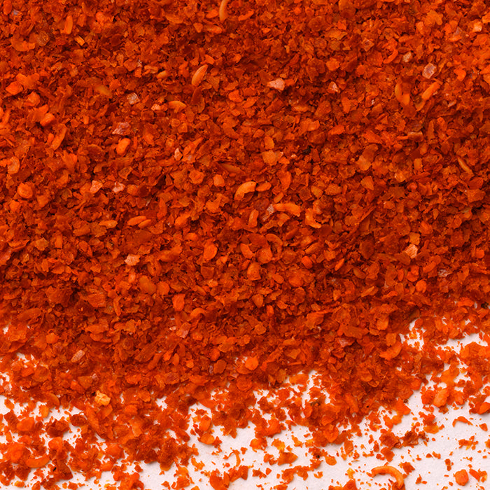 Close-up view of vibrant red Ichimi Togarashi Chili Crushed by Whole Spice Inc. scattered on a white surface.