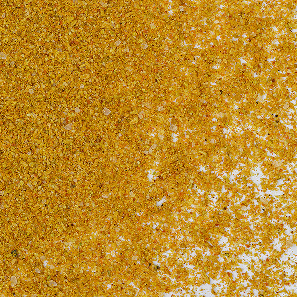 A close-up of Shawarma Spice Mix by Whole Spice Inc. shows yellow and orange granules scattered on a white surface, highlighting the coarse texture and vibrant colors typical of Middle Eastern seasoning blends.