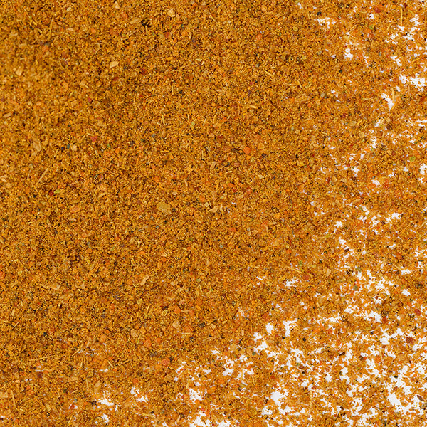 A close-up of Whole Spice Inc.'s Sri Lankan Curry Powder shows a scattered pile of fine, orange-brown curry spices with a slightly coarse texture and colorful flecks, perfect for authentic Sri Lankan dishes.