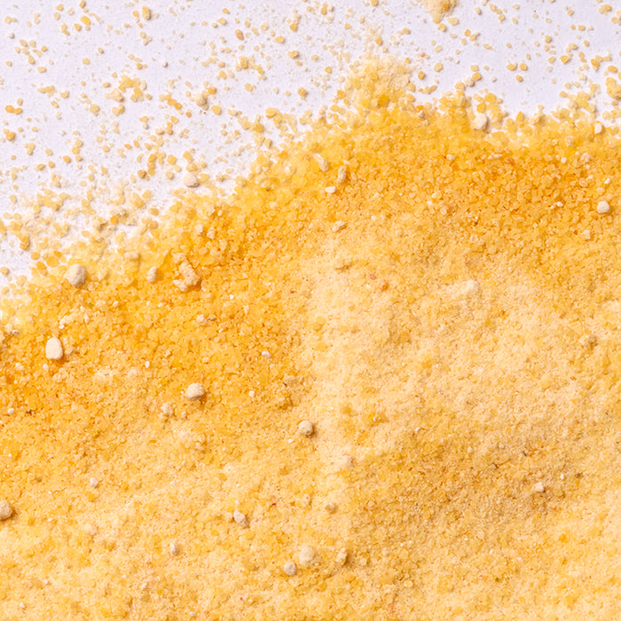 Close-up of Whole Spice Inc. Sweet Potato Powder and yellow cornmeal on a white surface, showcasing their fine and coarse granular textures.