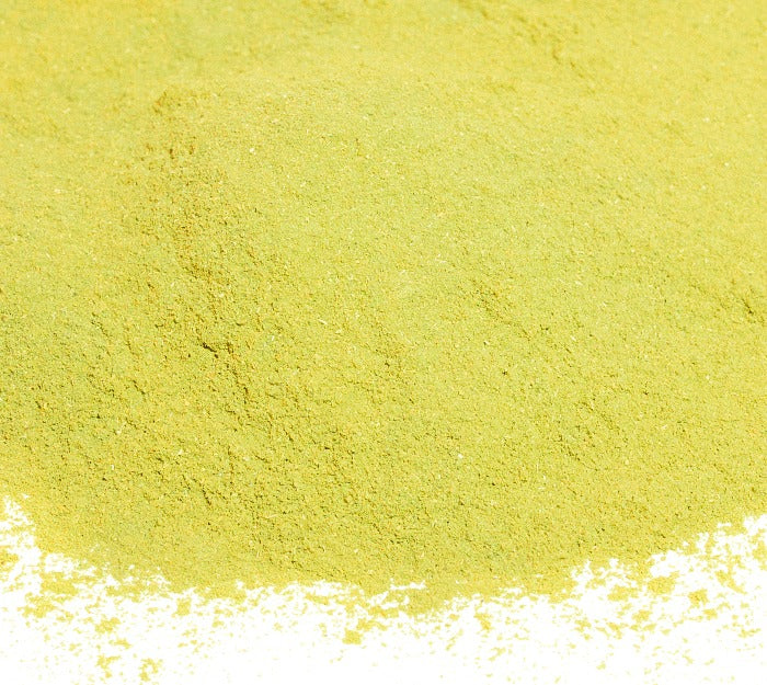 A pile of fine, light yellow-green Bay Leaves Ground from Whole Spice Inc. is spread across a white surface.