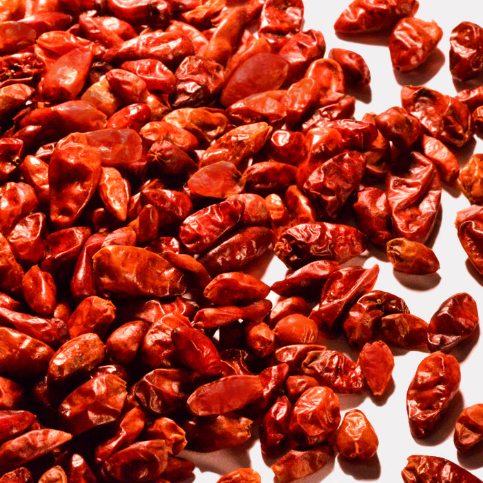 A close-up of Whole Spice Inc. Pequin Chili Whole—dried red hot chili peppers—scattered on a white surface.