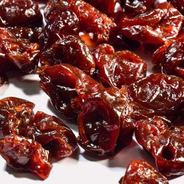 Close-up of glossy, dark red Dried Cherries by Whole Spice Inc. scattered on a white surface—ideal as healthy snacks or natural dried fruit for any occasion.