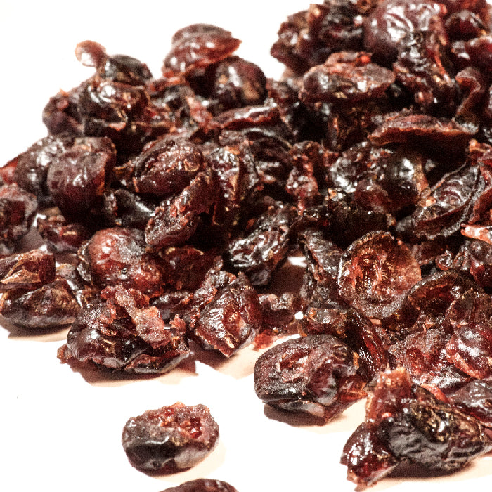 A close-up of Whole Spice Inc. Dried Cranberries scattered on a white surface shows their deep red, glossy, and wrinkled texture—ideal for smoothies or trail mixes.