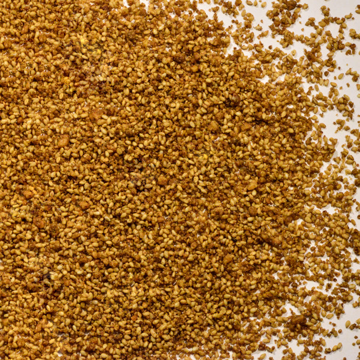 A close-up view of toasted sesame seeds, a key component in Dukka by Whole Spice Inc. The golden brown seeds are scattered on a white surface, highlighting their textured and uneven appearance.