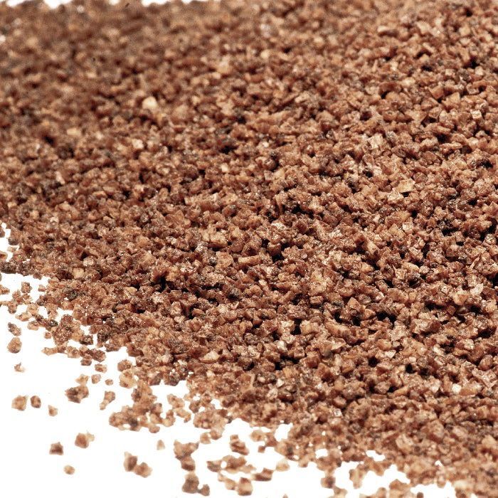 A close-up shows coarse, brown Espresso Sea Salt grains from Whole Spice Inc. scattered on a white surface.