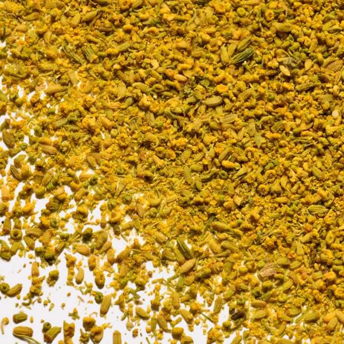 A close-up of Whole Spice Inc. Fennel Pollen displays its coarse, textured blend and aromatic fennel notes, scattered across a white surface.