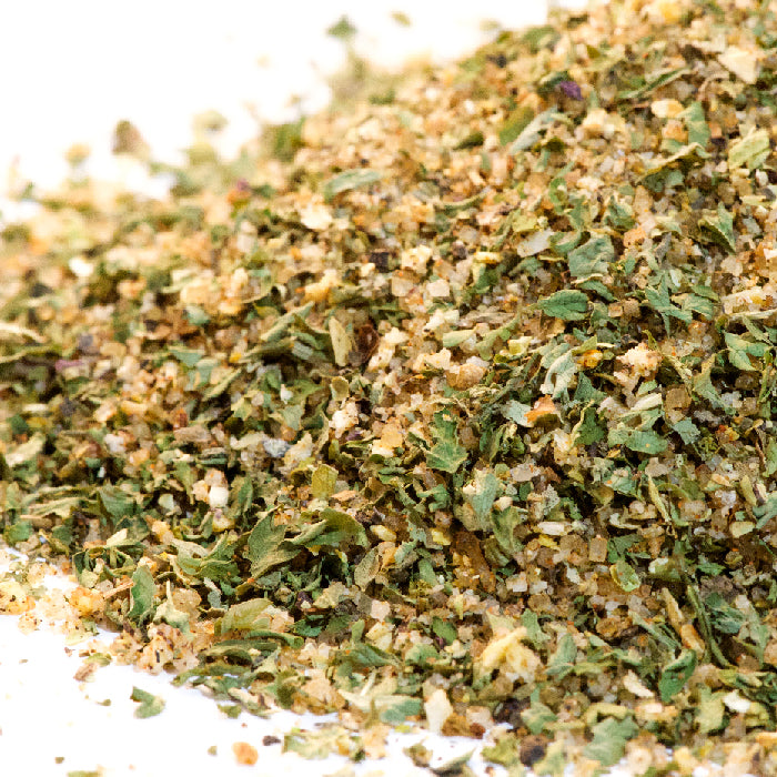 Close-up of Fish Seasoning by Whole Spice Inc.—a colorful blend of dried herbs and spices with green flakes and yellowish granules, perfect for enhancing a variety of dishes.