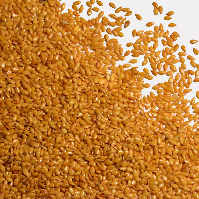 A generous layer of Whole Spice Inc. Flax Seeds Golden is scattered over the lower left corner of a white background, highlighting these heart-healthy seeds in their natural form.