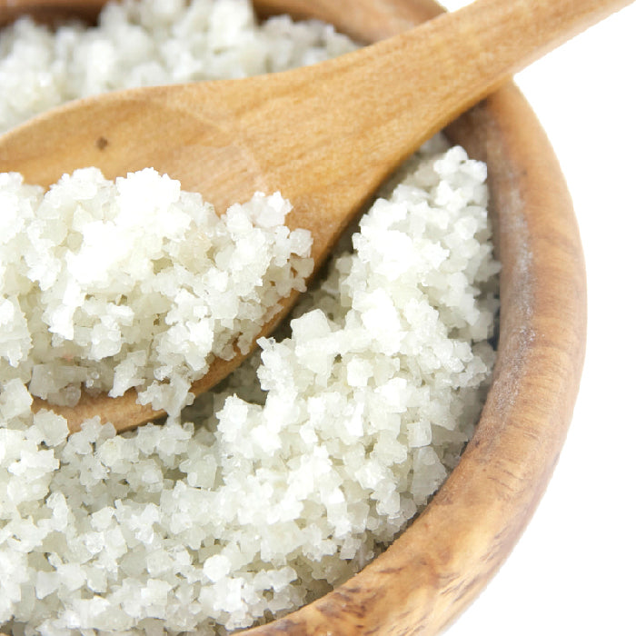 A wooden bowl filled with Whole Spice Inc. French Gray Salt, with a wooden spoon inside scooping up the mineral-rich crystals.