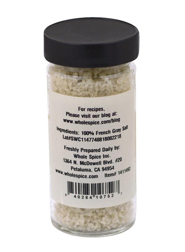 A clear glass jar with a black lid holds Whole Spice Inc.'s French Gray Salt, labeled as 100% Celtic sea salt. Company info and a recipe website are provided, making it perfect for use as a finishing salt.