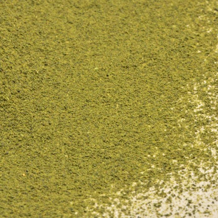 A close-up shows a generous amount of Whole Spice Inc. Sencha Green Tea Powder, finely ground and scattered unevenly over a pale surface.
