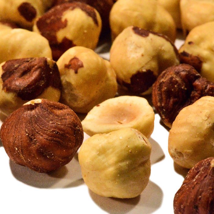 A close-up of Whole Spice Inc. Unsalted Roasted Hazelnuts, some with partially removed brown skins, arranged on a white surface.