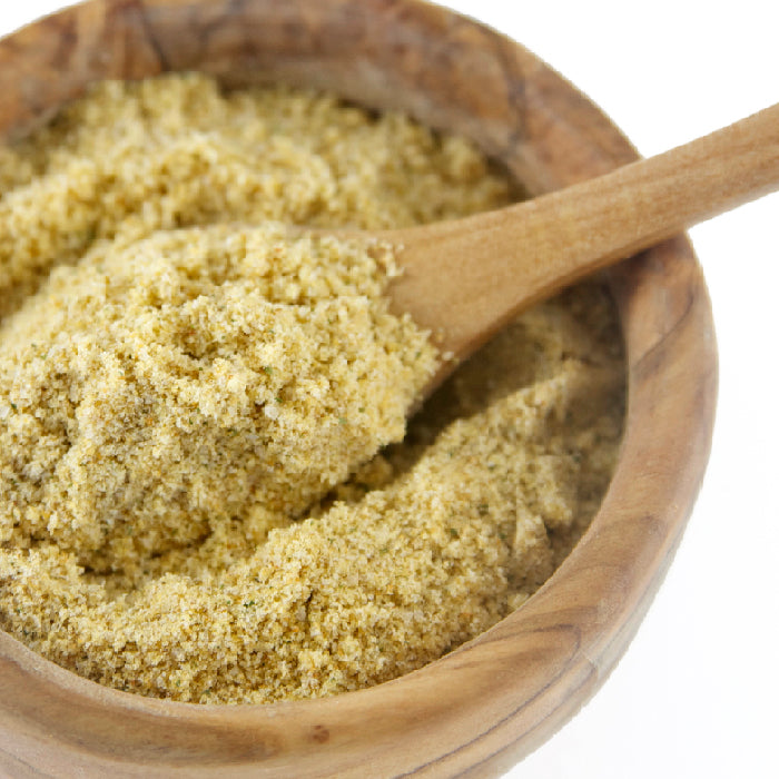 A wooden bowl filled with Whole Spice Inc. Hummus Spice Blend, with a wooden spoon scooping the light brown seasoning. The background is white.