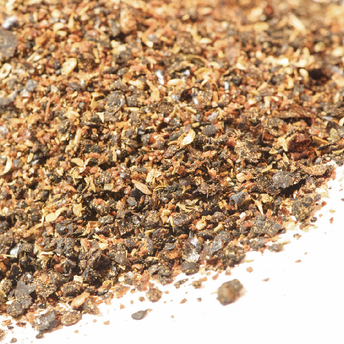 Close-up of ground black pepper in coarse and fine grains on a white surface—an excellent companion to Istanbul Salad Seasoning by Whole Spice Inc.