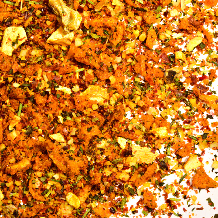 A close-up of Whole Spice Inc. Italian Pasta Seasoning, featuring dried garlic, fried onion, green herbs, and orange flakes scattered on a white surface for a burst of Italian flavor.