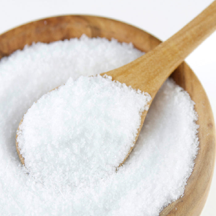 A wooden spoon scoops Whole Spice Inc. Kosher Salt from a wooden bowl against a white background, highlighting the salt’s pure, crisp flavor crystals.