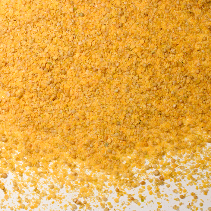 Close-up of Whole Spice Inc. Yellow Mustard Seed Coarse Ground, showing its coarse, granular texture scattered on a white surface—perfect for diverse culinary uses and adding robust flavor to your dishes.