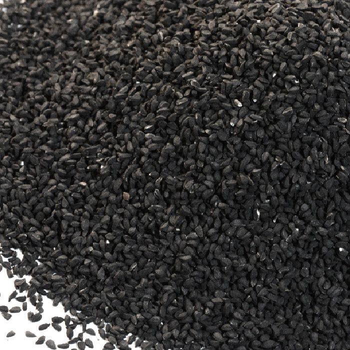 A close-up of Nigella Seed by Whole Spice Inc.—small, oval black seeds, some scattered—ideal for enhancing pickling spice or panch phoron blends.
