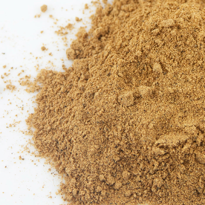 A close-up of Nutmeg Powder by Whole Spice Inc. shows its light brown, aromatic, and finely textured form with small clumps on a white surface—ideal for enhancing both sweet and savory recipes.