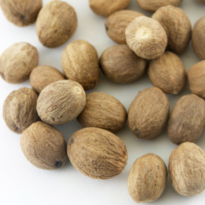 A close-up of Nutmeg Whole by Whole Spice Inc.—aromatic seeds with a rough brown surface scattered on white—ideal for enhancing sweet and savory dishes.