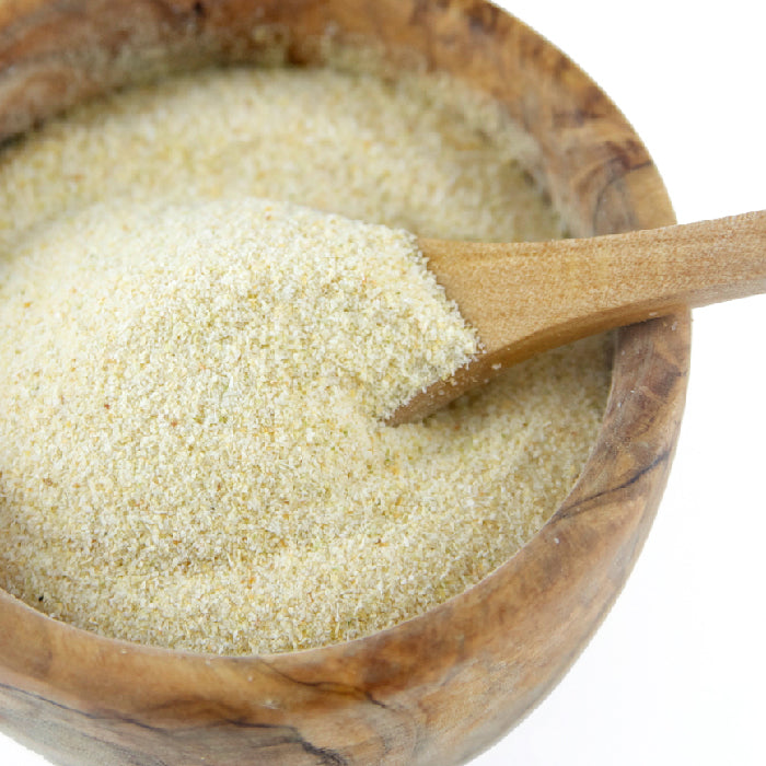 A wooden bowl filled with Whole Spice Inc. Onion Granulated, with a wooden spoon scooping some of the powder. The background is plain white.