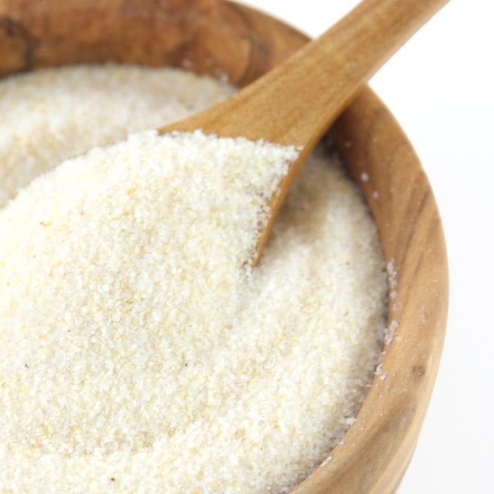 A close-up of a wooden bowl filled with Whole Spice Inc. Onion Salt, showing its fine blend as a wooden spoon scoops some out.