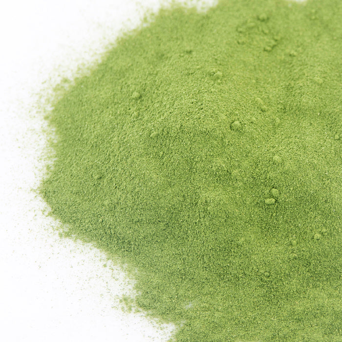 A close-up shows a small pile of fine, bright green Parsley Powder by Whole Spice Inc. on a white surface. The smooth, evenly textured powder is made from dried parsley.