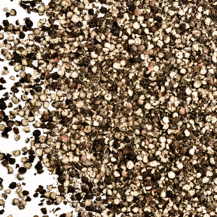 A close-up of Whole Spice Inc. Pepper Black Cracked Organic, scattered on a white background—ideal for seasoning your favorite dishes.