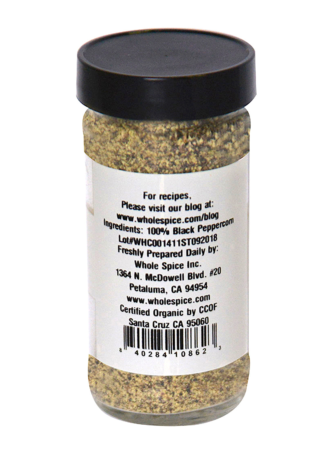 A clear jar of Whole Spice Inc. Pepper Black Ground #2 Organic with a black lid contains aromatic black pepper. The label displays ingredients, company info, website, certifications, and has a barcode at the bottom.