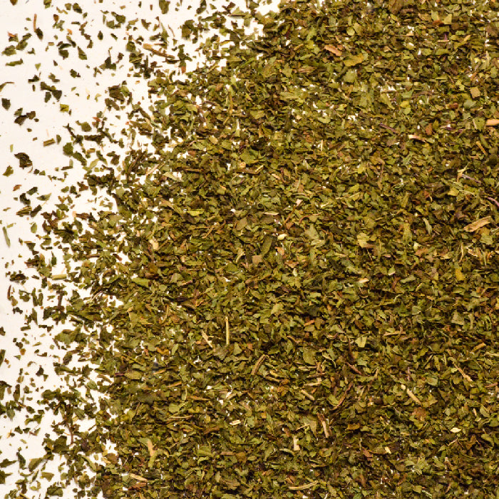 A close-up of finely chopped Whole Spice Inc. Peppermint Leaves scattered across a white surface, covering most of the right side of the image.