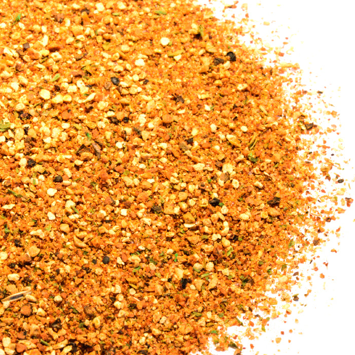 A close-up of Whole Spice Inc. Peri Peri Blend—a coarse, orange-red seasoning with herbs and bold African bird’s-eye pepper heat—piled on a white background.