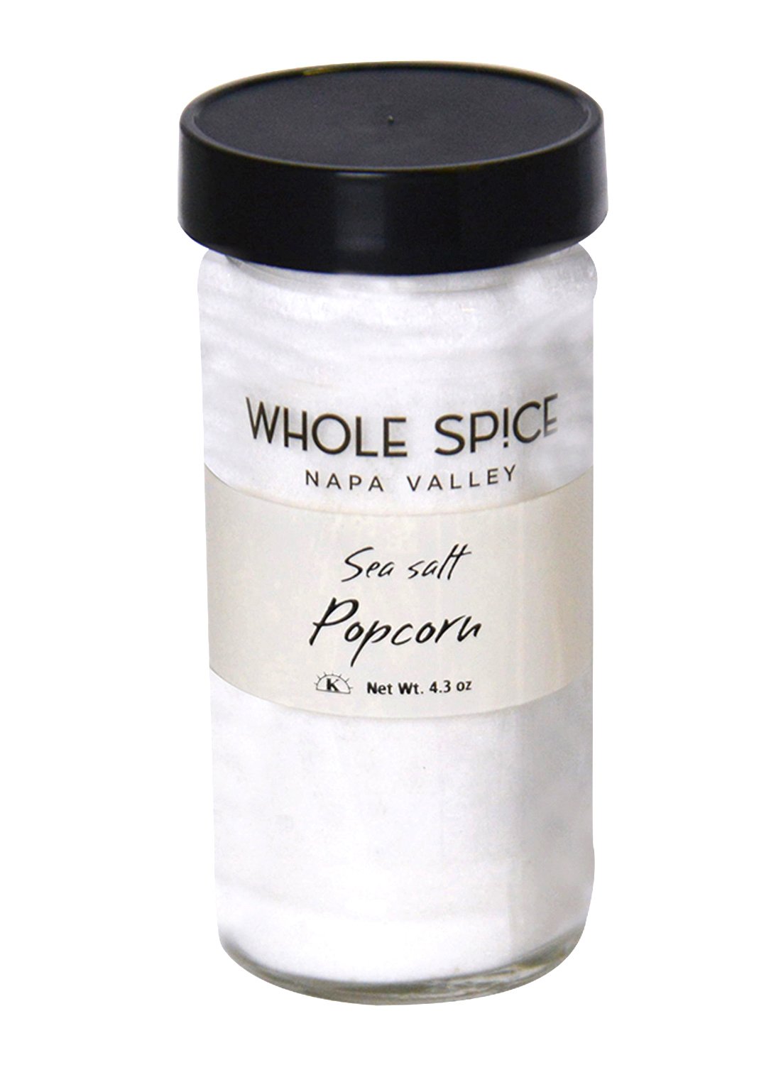 A clear glass jar with a black lid contains Popcorn Salt Fine by Whole Spice Inc. The label reads WHOLE SPICE NAPA VALLEY Popcorn Salt Fine, Net Wt. 4.3 oz.