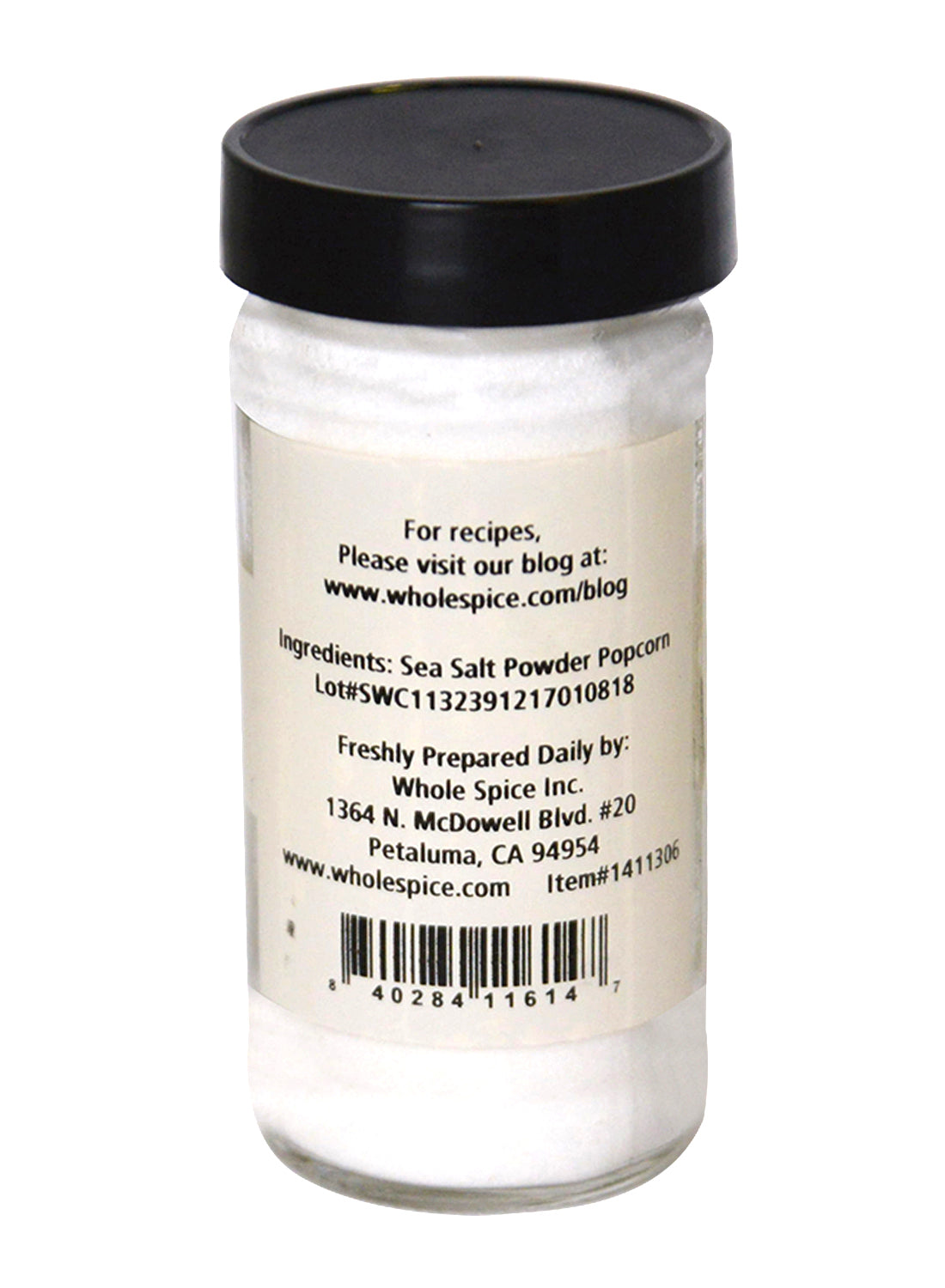 A clear glass jar with a black lid contains Whole Spice Inc. Popcorn Salt Fine. The label includes ingredients, company details, address, barcode, and a website with popcorn recipes.
