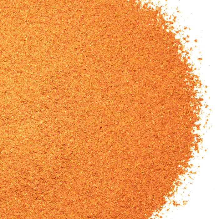 A close-up of Whole Spice Inc. Pumpkin Pie Spice—fine orange granules spread on a white background, creating a textured surface that's perfect for holiday baking.