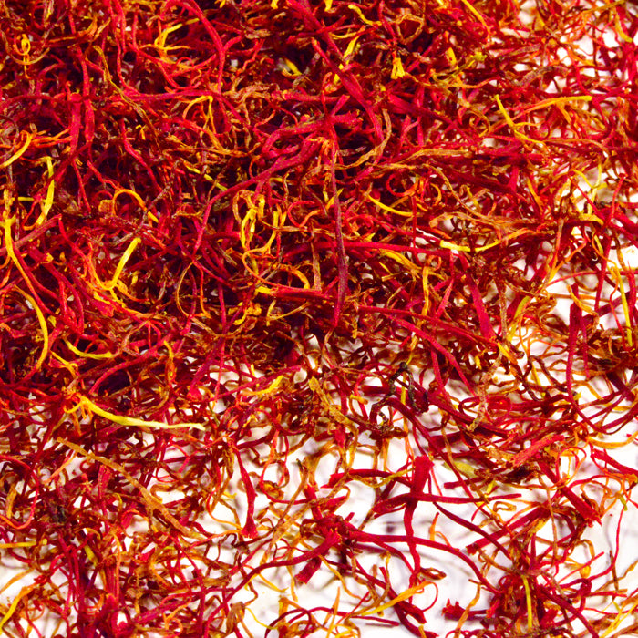 A close-up of Whole Spice Inc. Saffron showcases its vivid red and orange threads with delicate, thin, curly strands displayed against a white background.