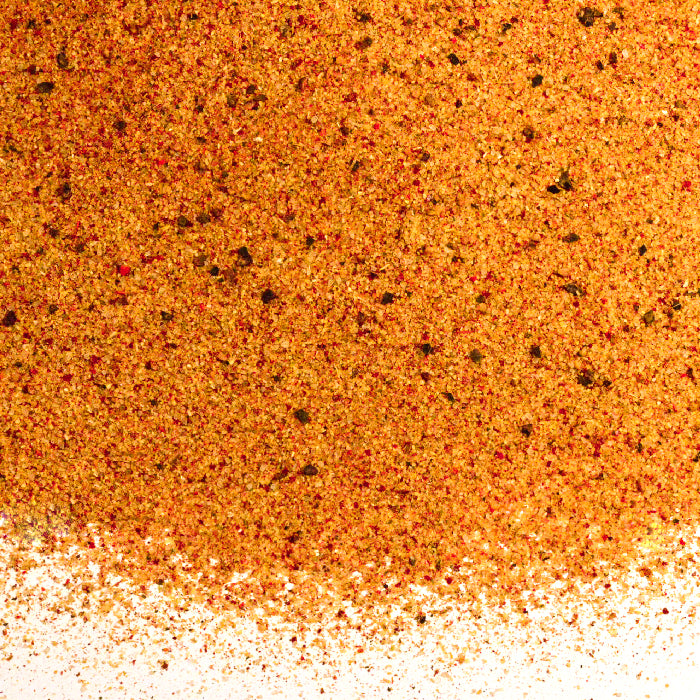 A close-up of Salt Seasoning by Whole Spice Inc. reveals a blend of fine orange, red, and brown granules with specks of herbs and pepper—ideal for enhancing your favorite recipes.