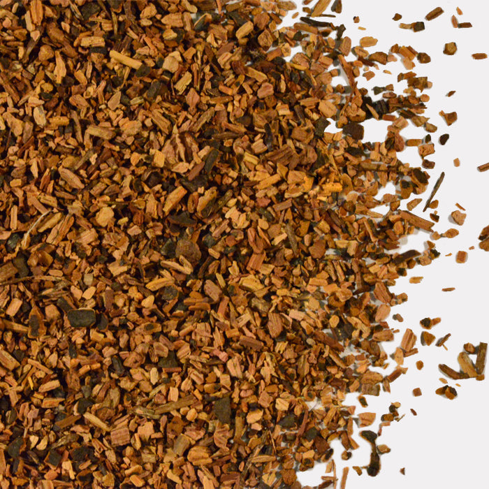 Close-up of coarse, brown Sarsaparilla Root Cut by Whole Spice Inc., granules scattered on a white background with a rough, irregular texture and unevenly spread small pieces.