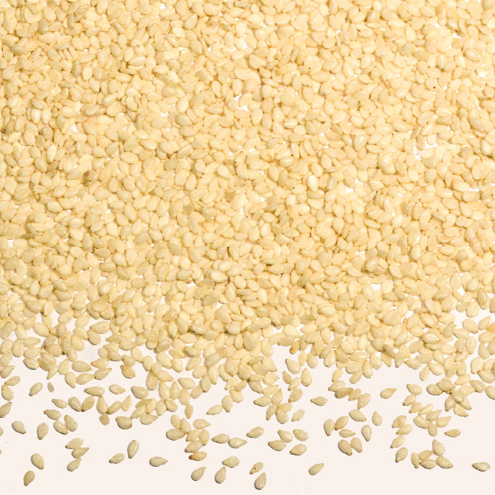 A generous heap of Whole Spice Inc. Sesame Seeds White Hulled is spread out on a white surface, densely packed at the top and gradually scattered toward the bottom.
